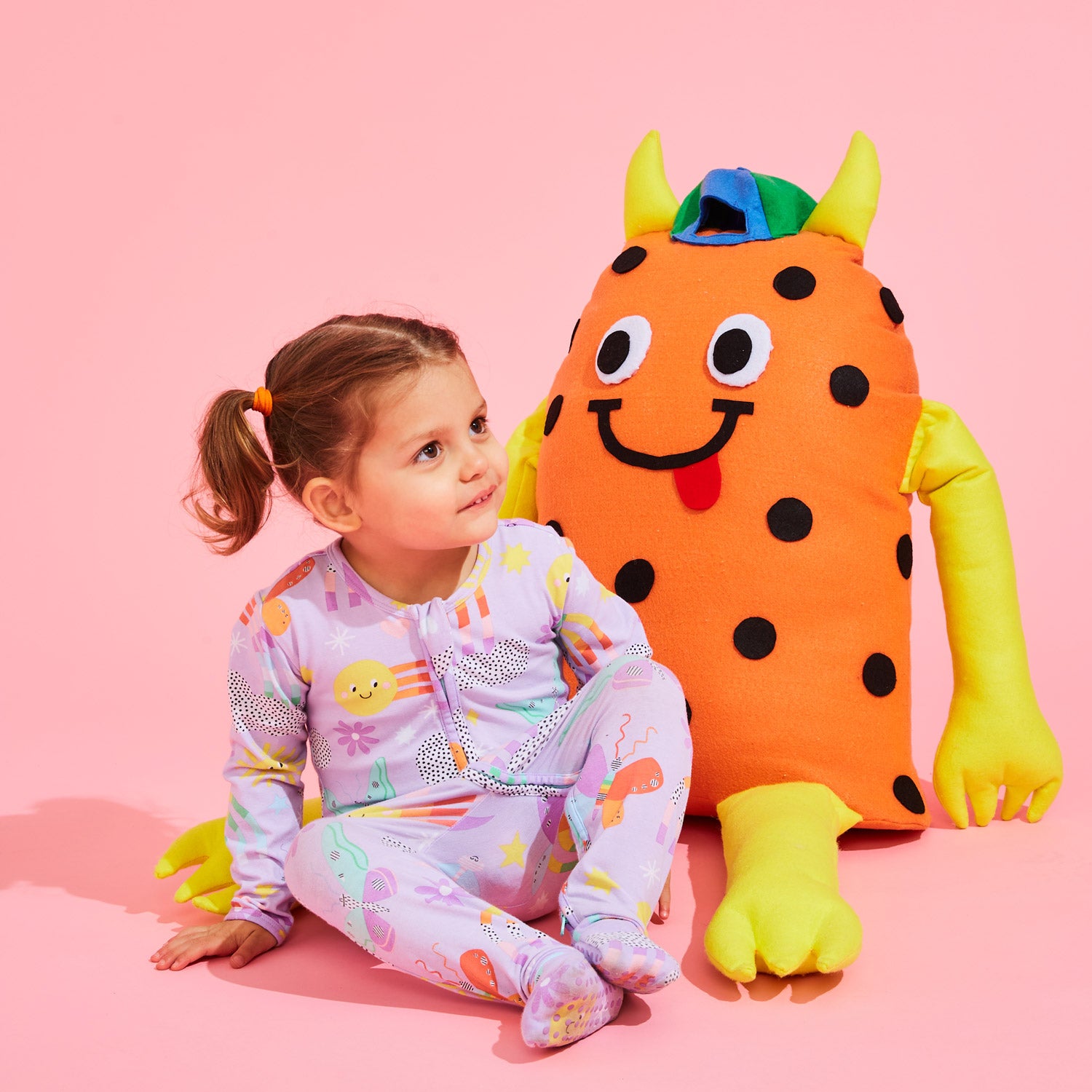 Children in patterned pyjamas play in a colourful background with custom Kitiya Palaskas cardboard props that include a sun, cactus, rainbow, clouds and butterfly