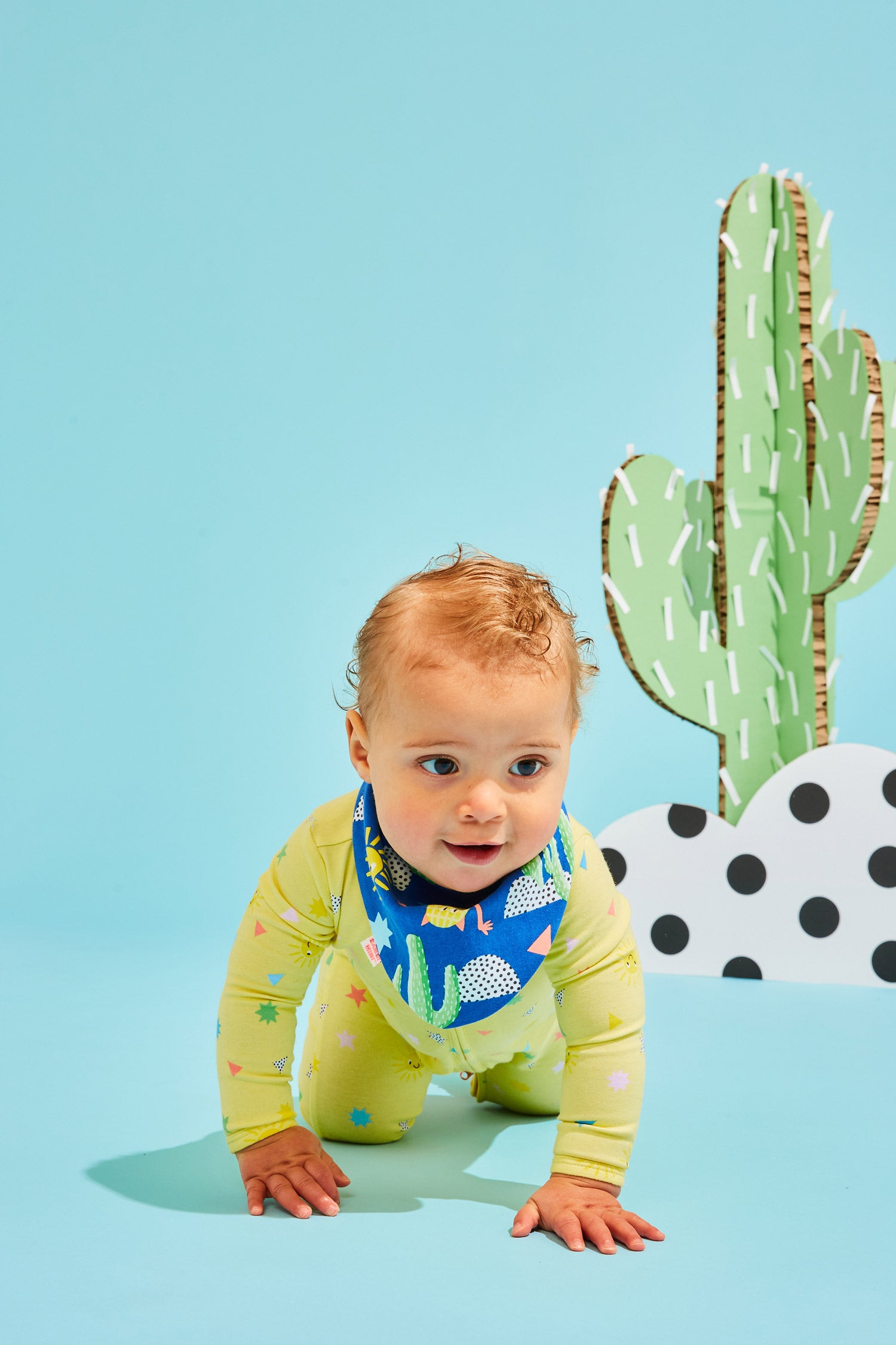Children in patterned pyjamas play in a colourful background with custom Kitiya Palaskas cardboard props that include a sun, cactus, rainbow, clouds and butterfly