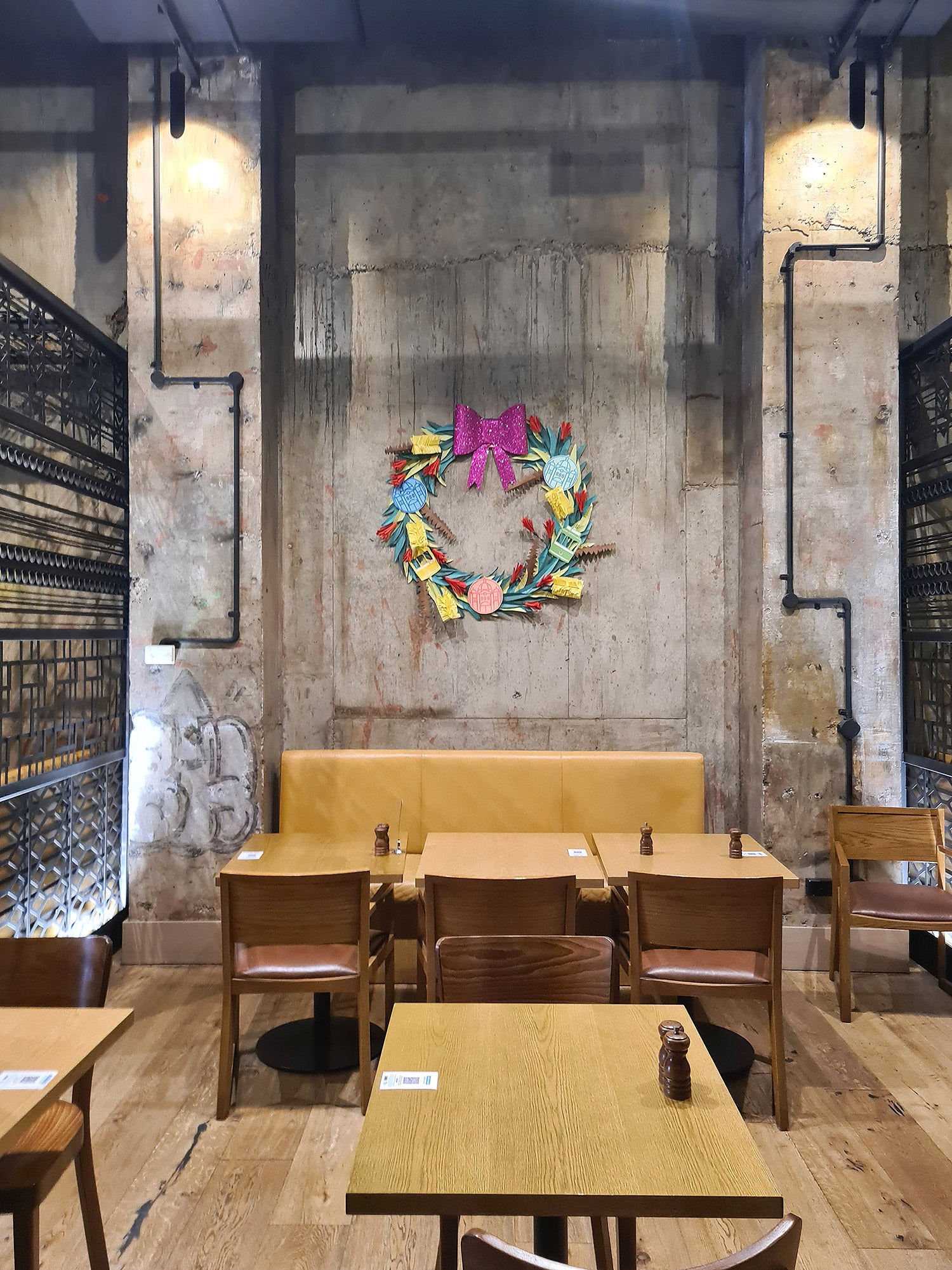 A giant handmade Papercraft Christmas wreath hangs on a concrete wall in a sleek, modern, hotel restaurant.