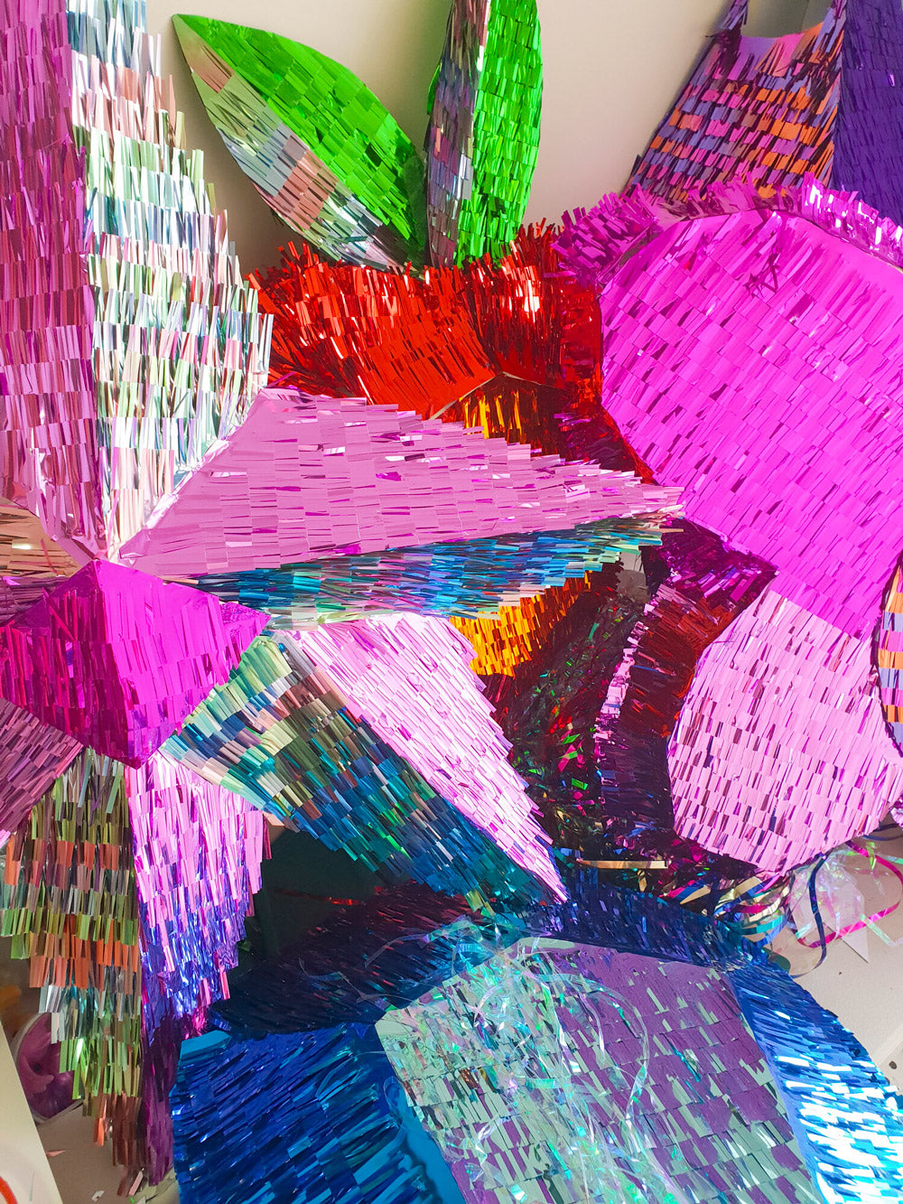 A close up photo of a collection of handmade metallic piñatas in rainbow colours.