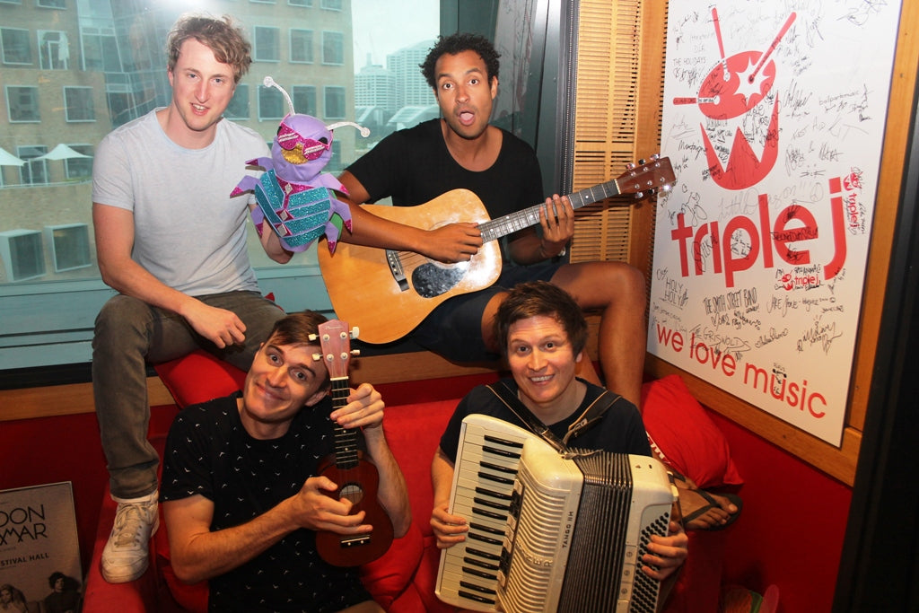 The Wombats, a band, poses at a publicity appearance with a colourful, glittery, handmade felt beetle puppet wearing glittery sunglasses.
