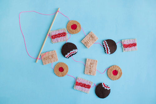 A hand-sewn felt mobile sits on a pale blue background. The mobile features various felt cookie motifs
