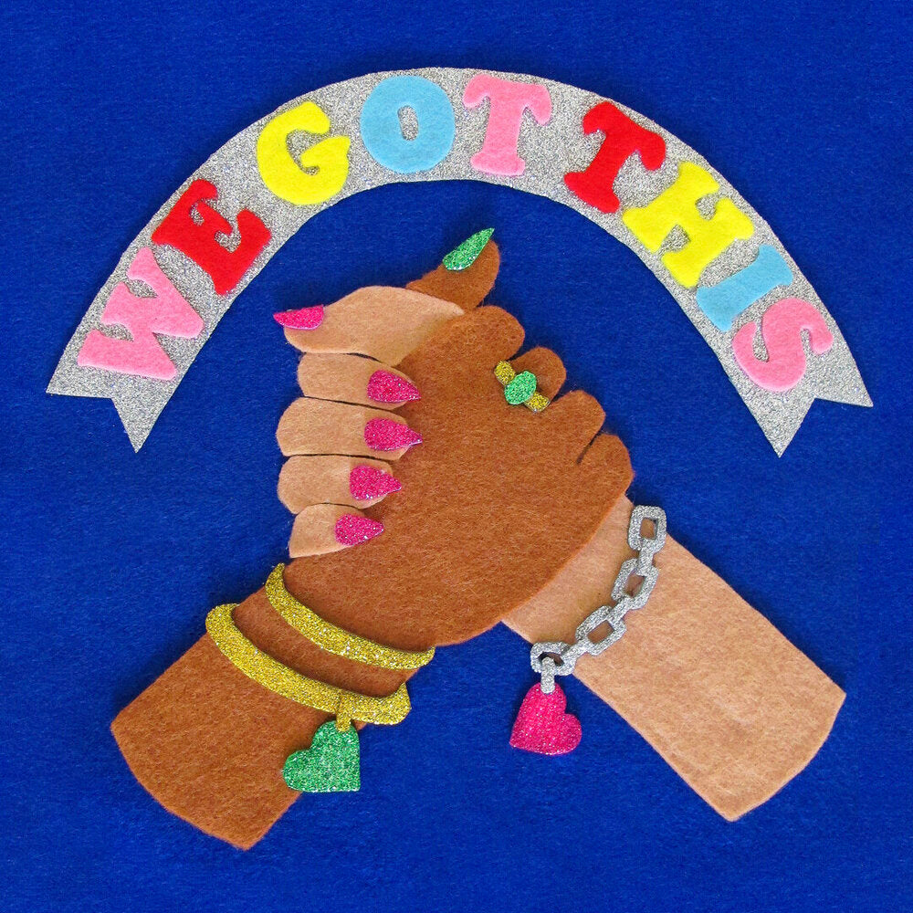 A felt collage illustration depicting two brown hands with long nails and glittery jewellery clasping each other and the words “We Got This” above in colourful text.