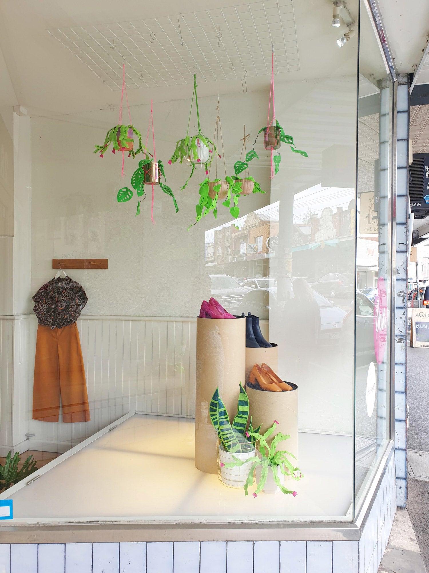 A collection of handmade felt indoor plant props in pots decorate the windows and shelves of a colourful clothing store.