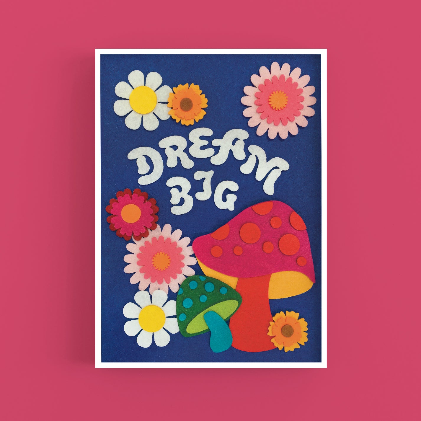 An A3 art print of a felt collage design. The design features felt flowers and mushrooms and the words Dream Big, on a blue felt background. The print is framed on a magenta background.