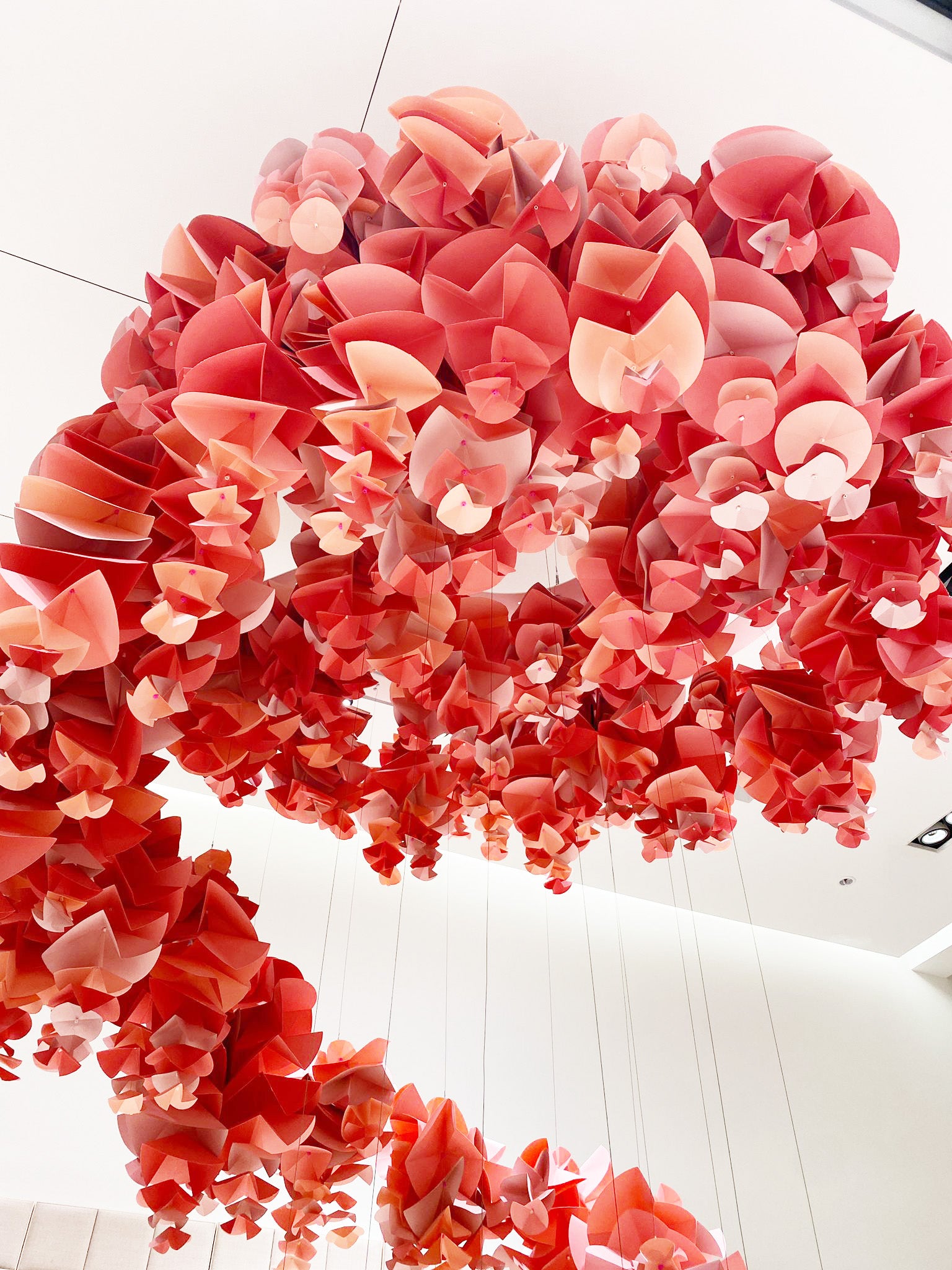 A large, pink, spiral-shaped papercraft petal installation hangs from the ceiling of a brightly lit retail store.