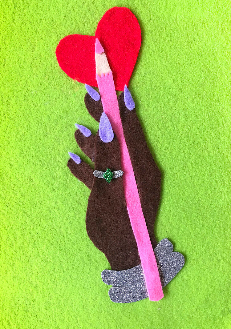 A felt collage illustration depicting a brown hand with long nails, holding a pink pencil. There is also a red heart motif and a green background.