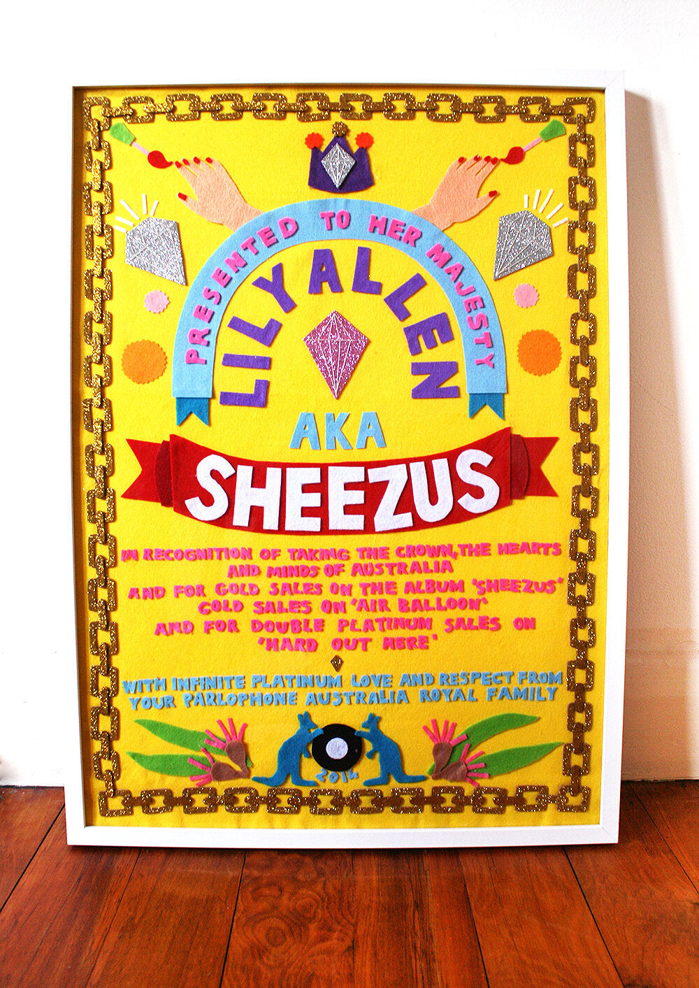 A colourful felt collaged artwork with a yellow background, and colourful motifs and words.