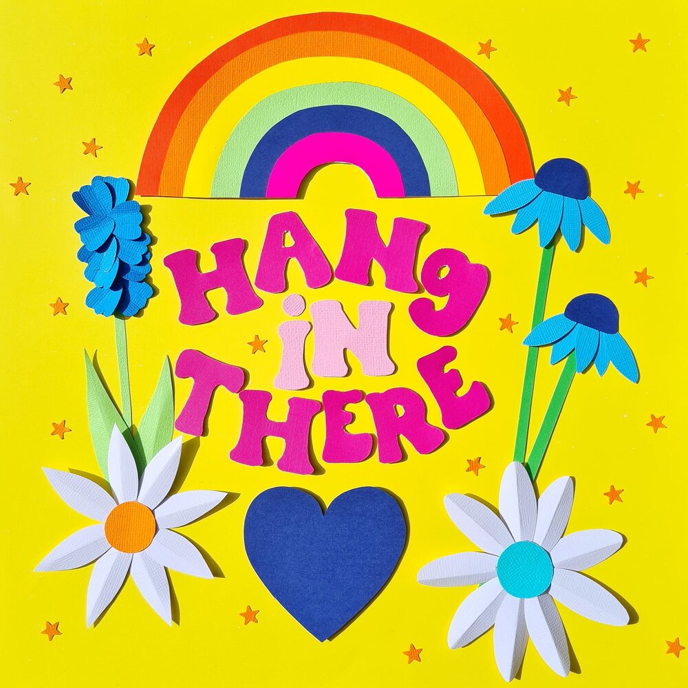 A papercraft collage illustration on a yellow background, depicting spring flowers, a rainbow, a blue heart and the words Hang In There in white text.