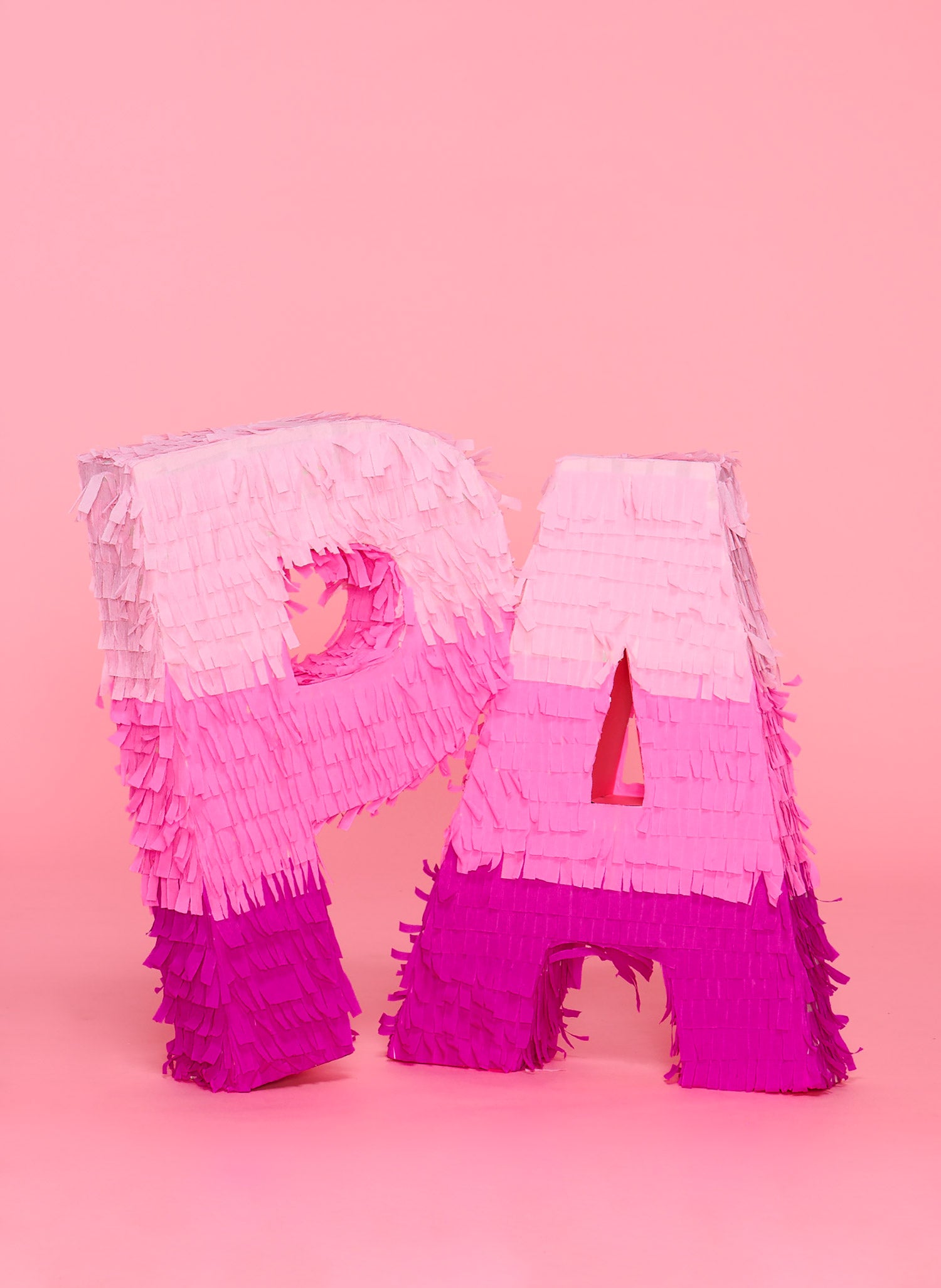 Two giant, oversized, handmade P and A shaped piñatas in 3 shades of pink sit against a pink background. 