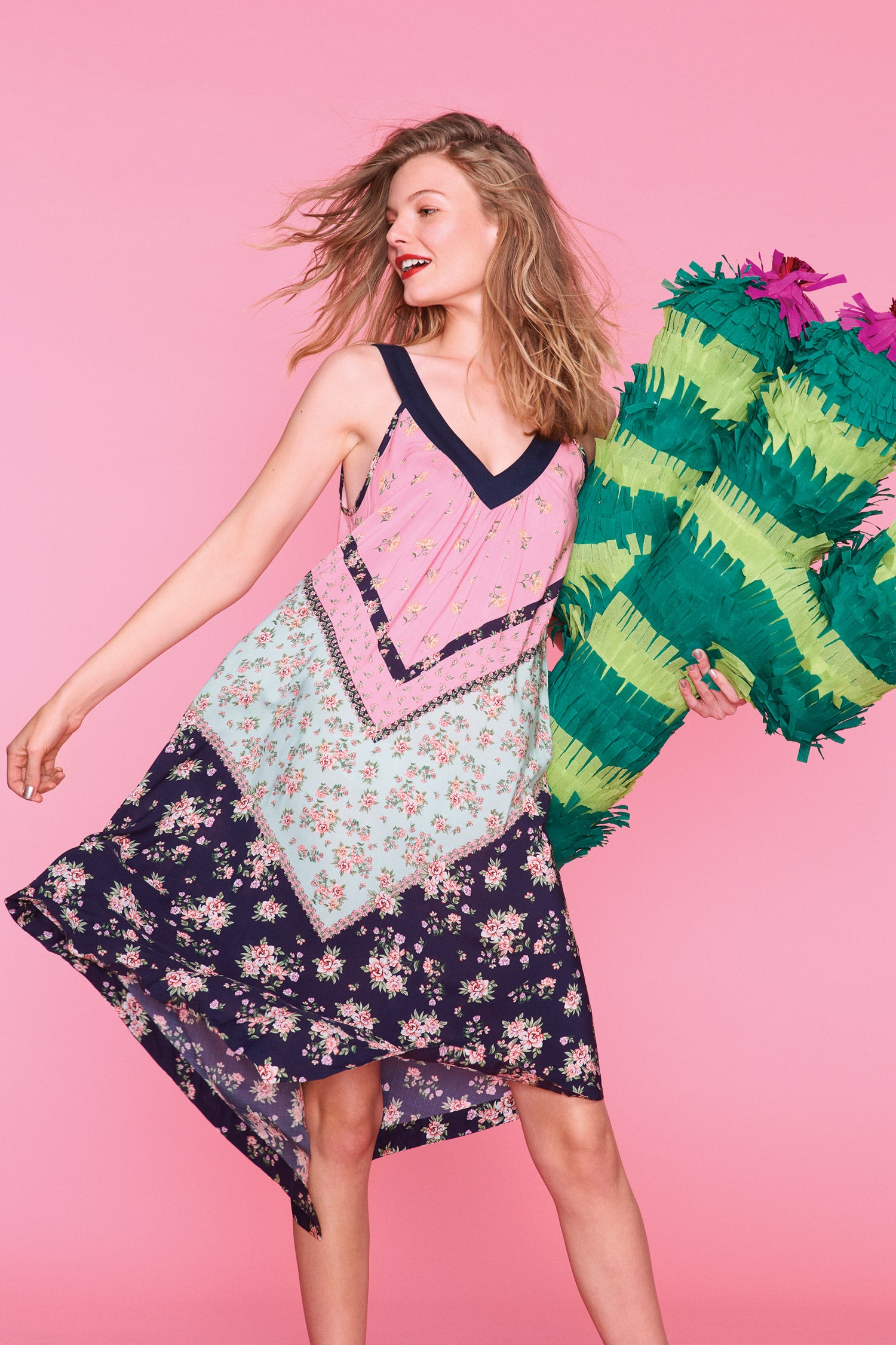 A woman in a colourful nightdress poses against a pink background with a giant, handmade, green cactus piñata.