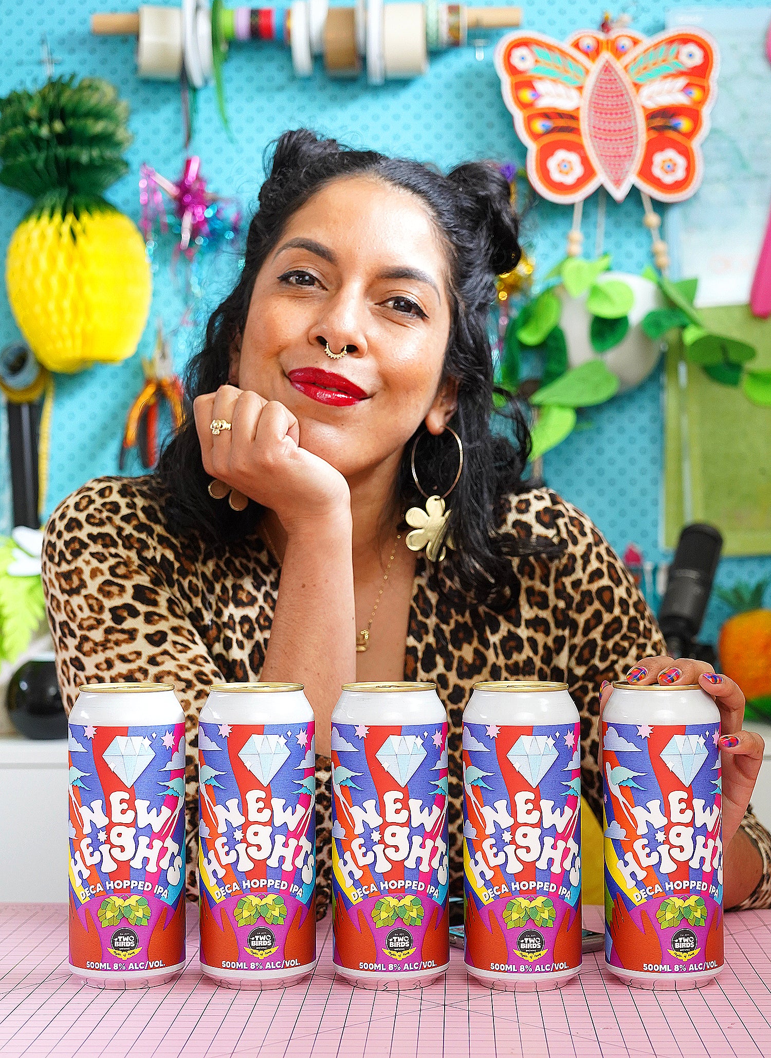 Kitiya Palaskas, a craft-based designer, poses in her studio with a collection of Two Birds Brewing beer cans with papercraft collage label designs. 