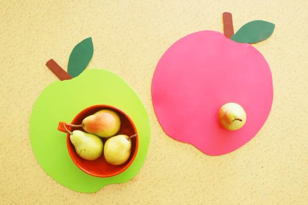 Two handmade wooden cut-out placemats in the shape of a red and a green apple sit on a yellow table. 