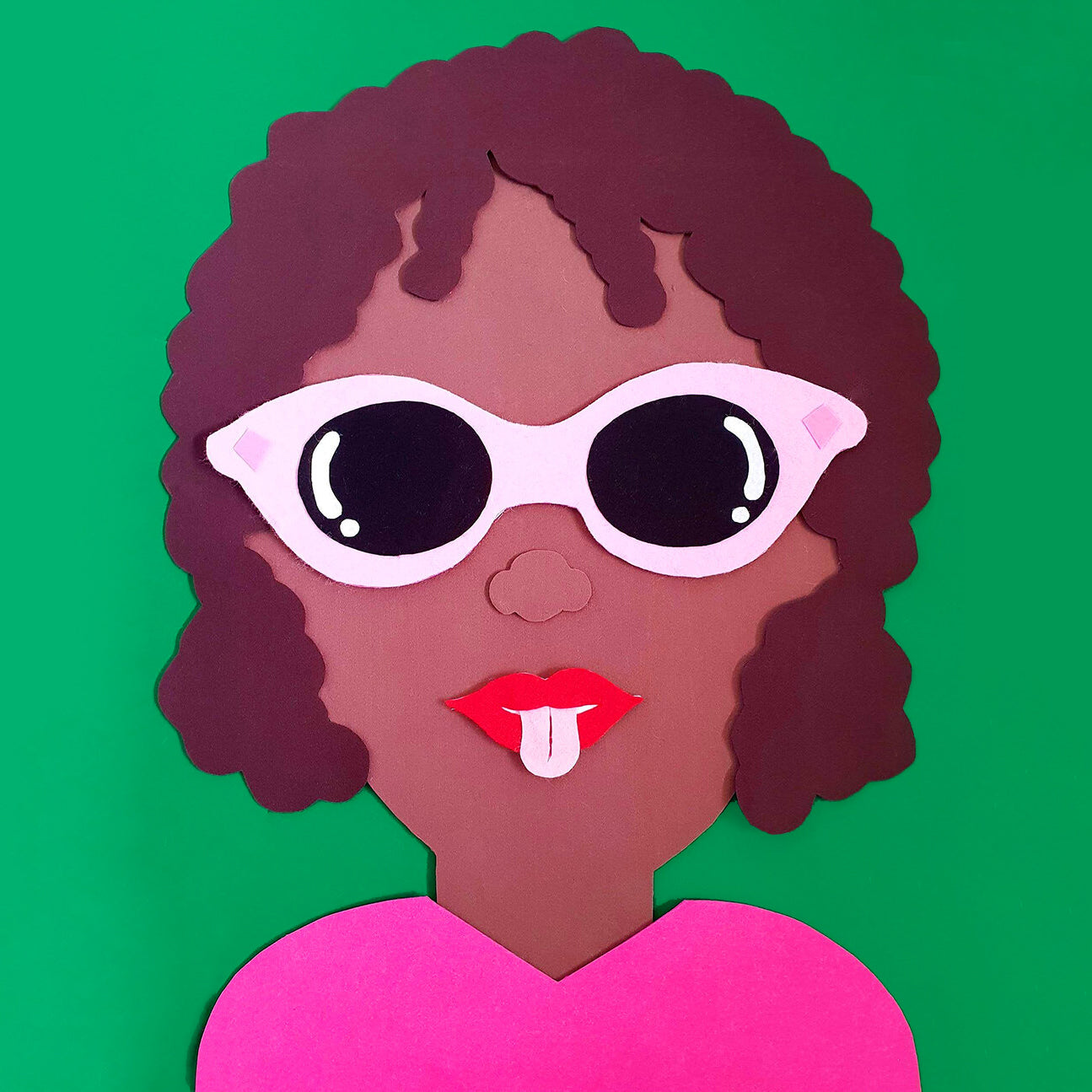 A felt collage installation of a brown woman with natural brown hair and pink sunglasses, on a green background 