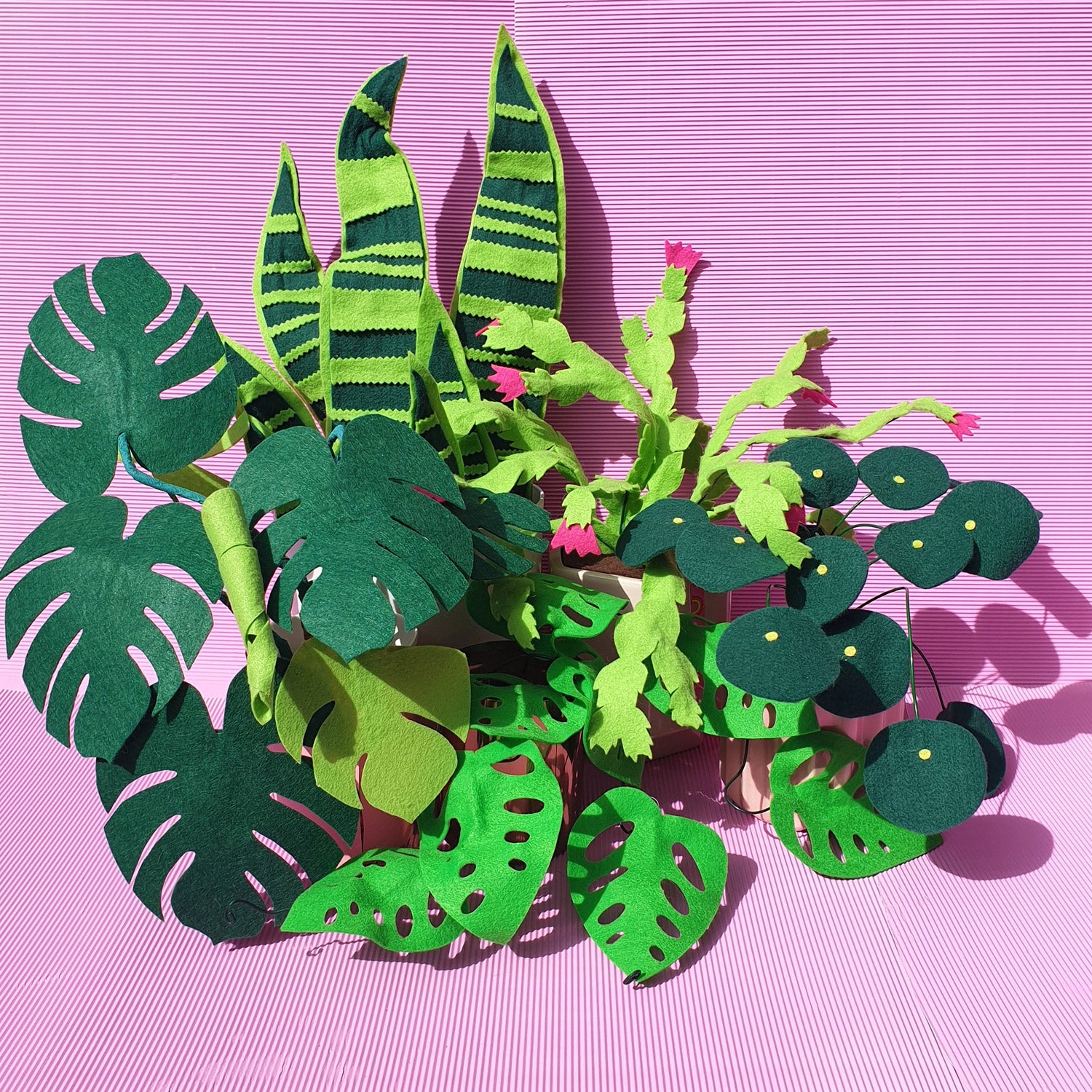 A collection of handmade felt indoor plant props in pots sit on a pink background.