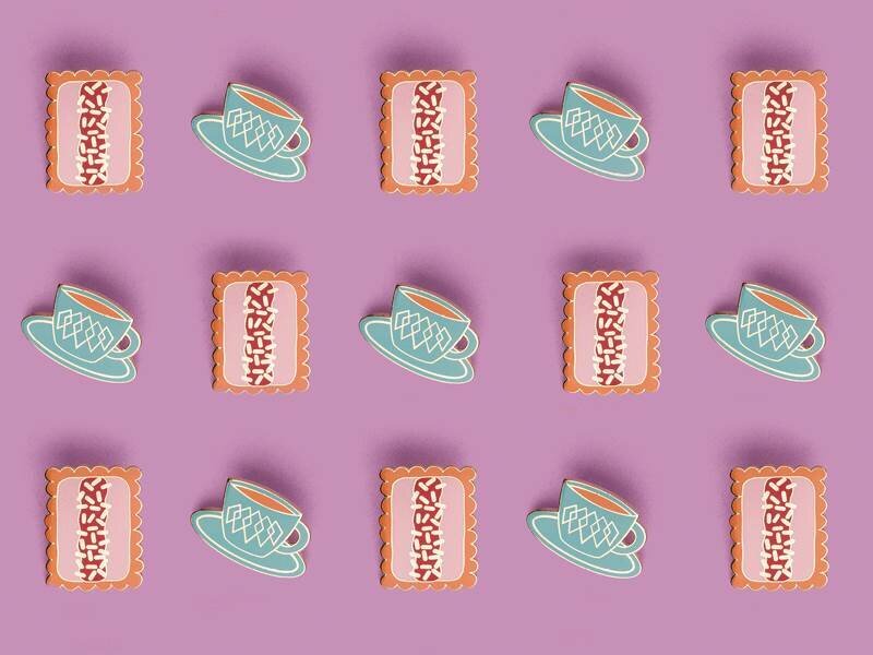 A collection of afternoon-tea enamel pins laid out in a diagonal grid formation on a purple background. One pin design is a cup of tea and one is a biscuit.