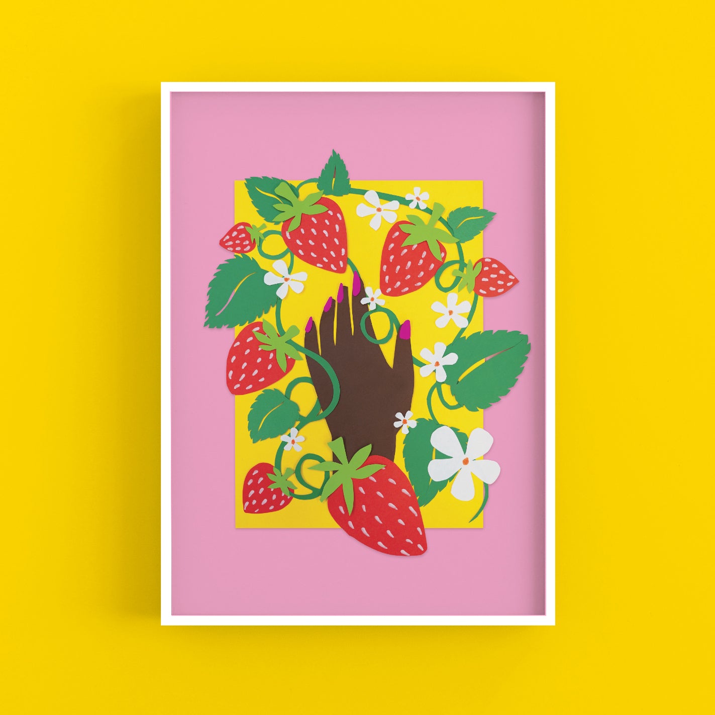 An A3 art print of a papercraft collage artwork. The print depicts strawberries and a brown hand with pink nail polish against a yellow and pink background. The print is in a white frame on a yellow background.